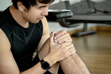 Asian sport man feeling knee pain or rheumatoid arthritis while sitting on the floor in fitness...