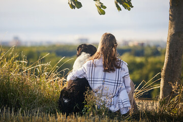 Teen girl sitting under tree with her dog. Rear view of pet owner and Czech Mountain Dog in nature..