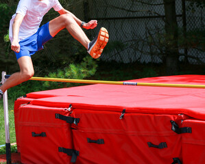 Teenage boy jumping over a high jump bar like he is hurdling