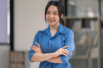 Portrait of happy asian woman smiling, posing confident, cross arms on chest, standing against office background