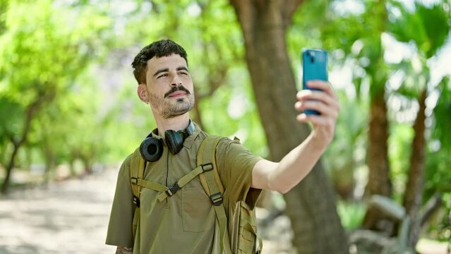 Young hispanic man tourist wearing backpack make selfie by smartphone at park