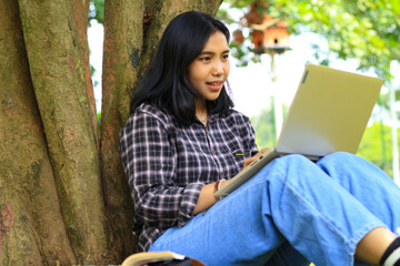 happy asian student using laptop and reading book to study for exam and surfing in the internet with excitement