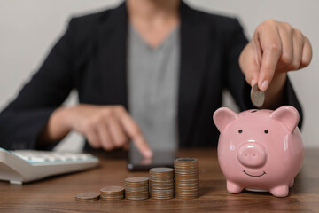 The thrifty businessman puts coins in a pink pig shaped savings box. The idea of saving money is to...