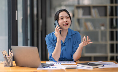 Cheerful business Asian woman freelancer making telephone call share good news about project working in office workplace, business finance concept.	