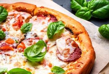 Homemade pizza with italian salami sausage, mozzarella cheese, tomato sauce and green basil on black kitchen table background, top view
