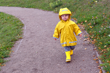 Little boy wearing yellow rain coat walking in the park
