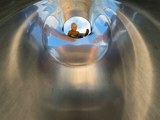 Little boy climbing inside metal pipe slide