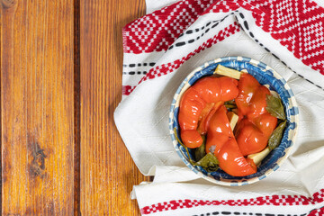 Red bell peppers pickled in Romanian traditional clay bowl and traditional towel on wooden table