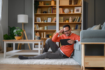 Smiling handsome entrepreneur working over digital tablet while sitting on carpet at home office