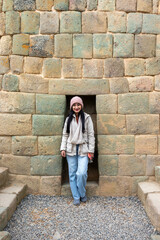 Mujer joven abrigada parada frente a una pared de piedras incas  - obrazy, fototapety, plakaty