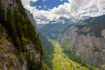 Aerial Drone View of The Swiss Alps with Buildings Sitting Along the Hills and Snow Covered Mountains in the background in Switzerland in Summer