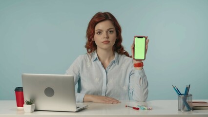 Medium isolated shot of a young woman looking at the camera and holding a phone with advertising area, workspace mock up.
