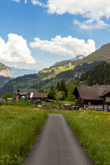 Fototapeta na wymiar Road Passing By Buildings in the Swiss Alps in Switzerland in the Summer With Mountains Peaking Through the Clouds in the Background