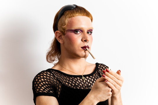 A red-haired non-binary person is posing on a white background. The man looks at the camera while lighting a cigarette. Concept of people is not identified with any gender.