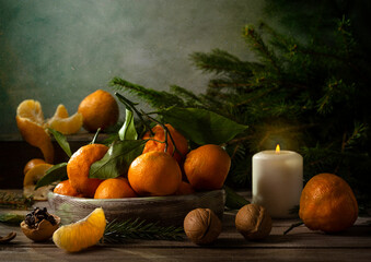 Christmas tangerines and fir branches on a wooden table. Fir branches and a candle create a holiday...