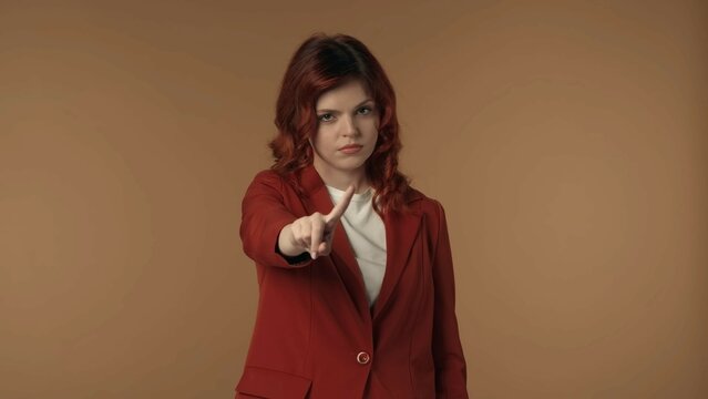 Medium isolated shot of a young woman pointing at the camera and negatively wagging her finger to show her disagreement, complaint about something.