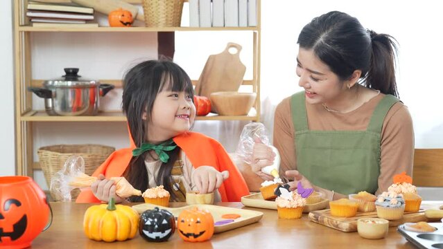 Happy of Mother and Daughter are Decorate Cupcakes Together in Kitchen at Home. Family Relations of Mom and Girl in Leisure Activity with feel happy halloween concept