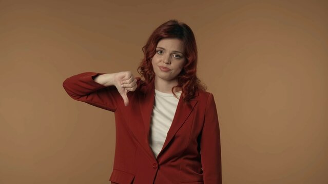 Medium isolated shot of a young woman looking at the camera and giving thumbs-down to show her disagreement, complaint about something.