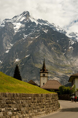 Road Leading to a Church of the Swiss Alps in Switzerland in the Summer with Mountains Peaking Through Clouds in the Background