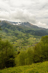 Buildings Sitting Along a Hill of the Swiss Alps in Switzerland in the Summer with Mountains Peaking Through Clouds in the Background