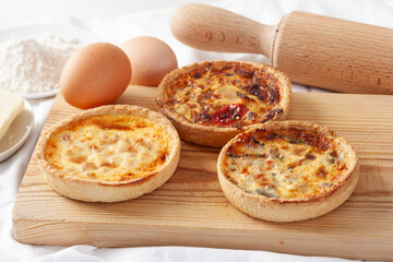 Freshly made savory mini cheese and vegetable quiches on a wooden board.