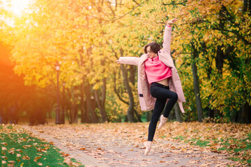 Fototapeta na wymiar Woman ballerina in pointe shoes in golden autumn park, standing in beautiful pose on yellow leaves