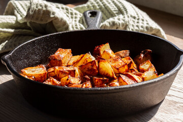 Fried diced potatoes in a cast iron frying pan. On a wooden chopping board in a kitchen