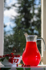Morse in a glass jug and red currant berries in a vase on the table by the window of the village kitchen © Нелли Овчинникова