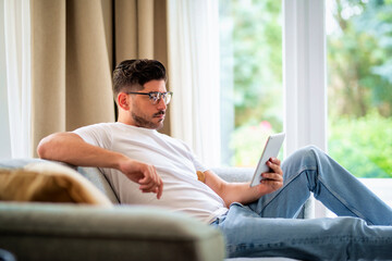 Middle-aged man sitting at home on the sofa and holding digital tablet in his hand