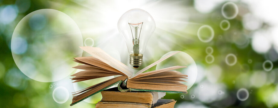  light bulb over an open book is a symbol of the concept of knowledge, learning and inspiration. Light bulb and open book on green blurred background