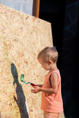 A little blond boy paints the wall with a roller.A kid in a T-shirt, shorts in the image of a...