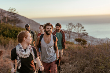 Young and diverse group of people and hikers hiking on a ridge overlooking the ocean and a beautiful sunset in South Africa