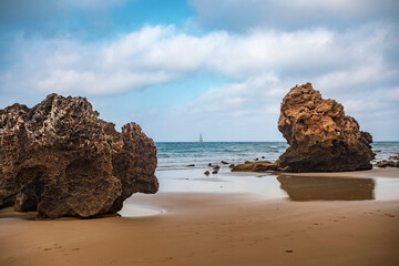 Natural beach with rocks and sailboat on the horizon of Bolonia, Cadiz, Andalucia, Spain