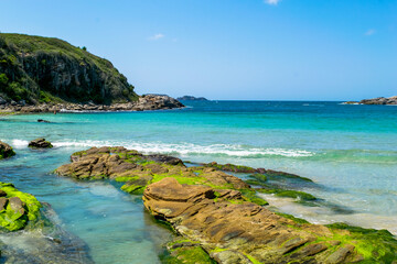 View of Praia das Conchas, close to the city of Cabo Frio, with blue sea around, undergrowth, rocks with green moss and mountains in the background - 132