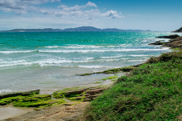 View of the beautiful Praia das Conchas, close to the city of Cabo Frio, with the blue sea around, undergrowth, rocks with moss and mountains in the background - 133