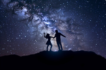 Fototapeta premium Silhouette of a Romantic couple Dancing on top of mountain and looking at starry sky.