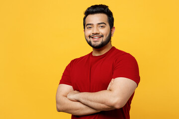 Side view young smiling happy fun Indian man he wearing red t-shirt casual clothes hold hands crossed folded look camera isolated on plain yellow orange background studio portrait. Lifestyle concept. - obrazy, fototapety, plakaty