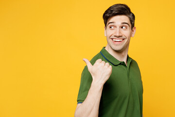 Young smiling happy man wears green t-shirt casual clothes point thumb finger aside indicate on workspace area copy space mock up isolated on plain yellow background studio portrait Lifestyle concept