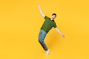 Fototapeta na wymiar Full body side view young happy man he wearing green t-shirt casual clothes look camera with outstretched hands arms leaning back stand on toes isolated on plain yellow background. Lifestyle concept.