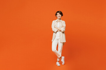 Full body young smiling cheerful happy caucasian woman wear beige shirt casual clothes look camera hold hands crossed folded isolated on plain orange red background studio portrait. Lifestyle concept.