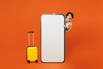 Traveler woman hold bag suitcase big huge blank screen mobile cell phone isolated on plain orange red background. Tourist travel abroad in free spare time rest getaway Air flight trip journey concept