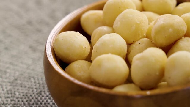 Shelled salty macadamia nuts in wooden bowl. Nutritious diet food. Rotation