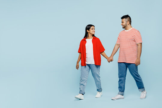 Full body side view young couple two friends family Indian man woman wear red casual clothes t-shirts together hold hands walk go strolling isolated on pastel plain light blue cyan color background. - Powered by Adobe