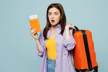 Traveler sad woman wear casual clothes hold passport ticket bag isolated on plain pastel blue background studio. Tourist travel abroad in free spare time rest getaway. Air flight trip journey concept.