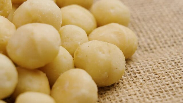 Shelled macadamia nuts on a rough rustic burlap. Nutritious diet food. Rotation. Macro shot