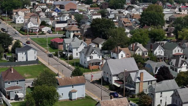 A slow forward zoomed aerial establishing shot of a typical middle-class rust belt residential neighborhood in summer. Densely packed homes. Pittsburgh suburbs.  	