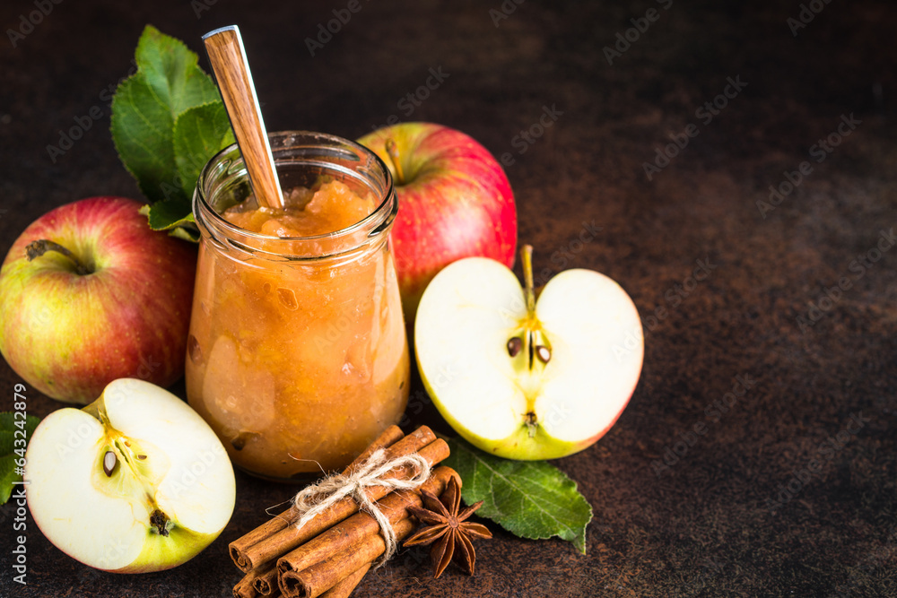 Wall mural apple jam with spices in glass jar and fresh apples on dark stone background.