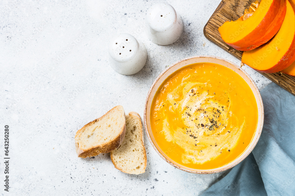 Wall mural Pumpkin soup puree with cream in the bowl. Top view image at white table.