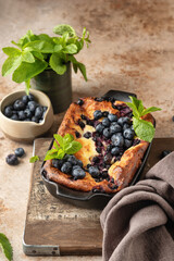 Cottage cheese casserole with blueberries and mint leaves deciration in baking dish on brown textured background