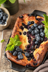 Cottage cheese casserole with blueberries and mint leaves deciration in baking dish close up on brown textured background